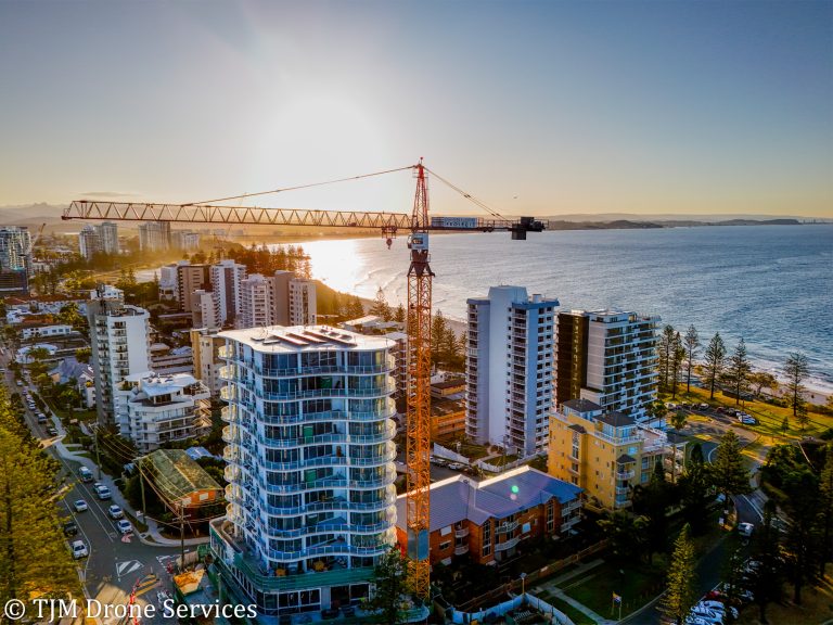 Aerial view of coastal cityscape with construction crane at sunset, showcasing drone services, real estate drone footage and construction progress using a drone